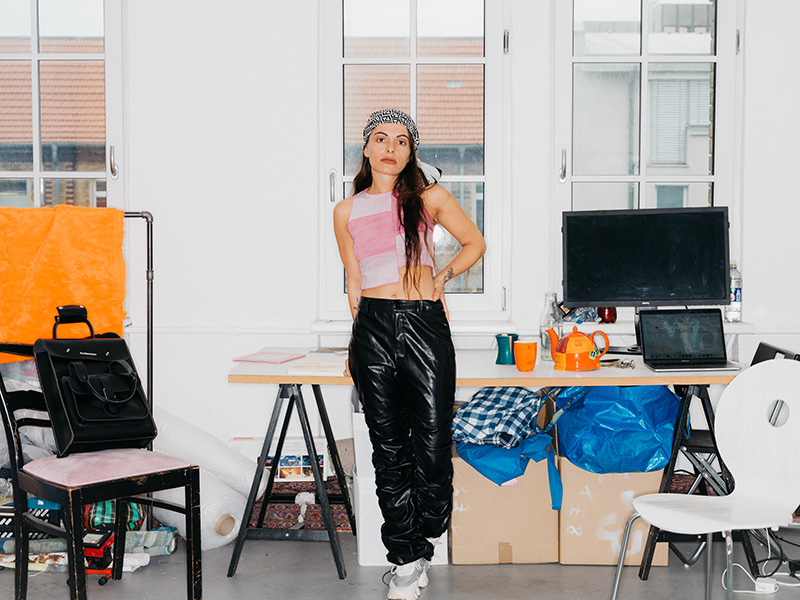 Young woman in bandana and with long hair stands in front of a desk in a studio space.