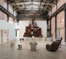 an installation of found wooden furniture piled into a sculptural form in a large warehouse-turned-museum