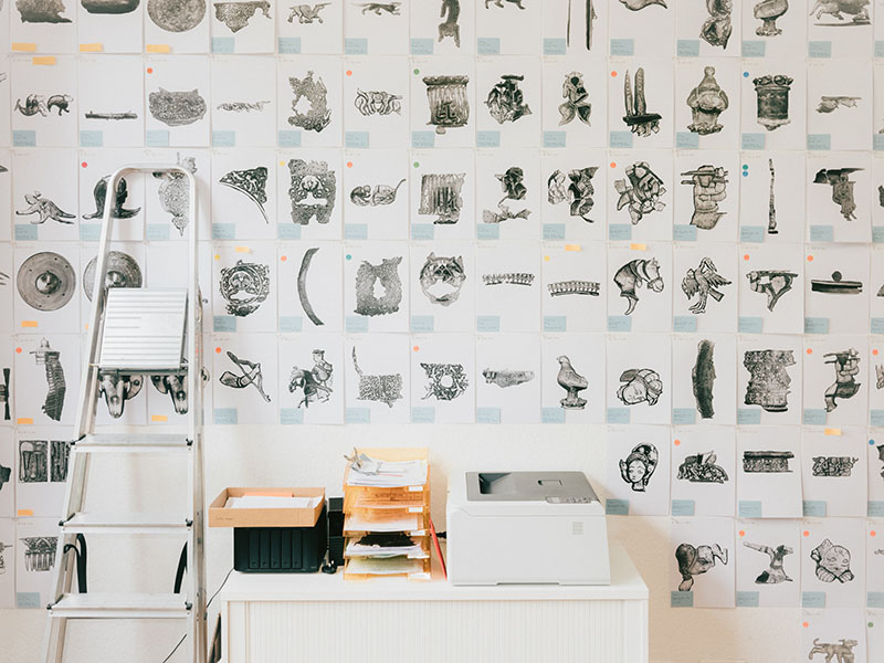 many photocopied images hanging in a grid on a wall with a ladder leaning on them