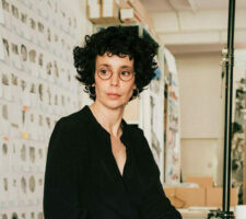 Artist Ilit Azoulay sitting on a small step ladder in her studio