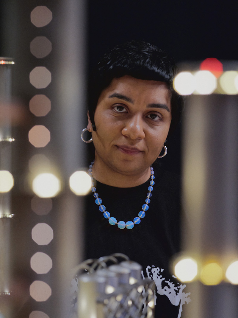 A portrait of Monira Al Qadiri behind out of focus lights