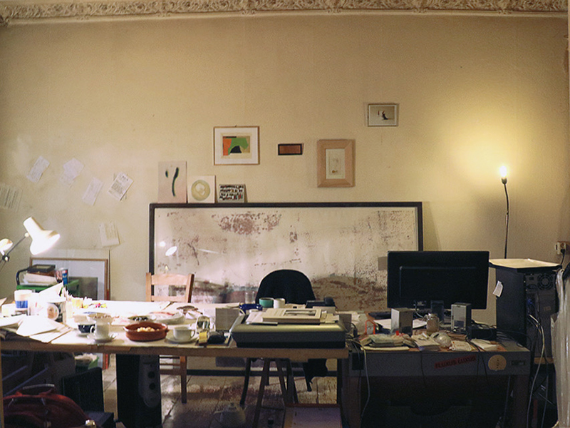 a massive desk in a big room with framed prints on the wall behind it. the desk is covered in materials and notes