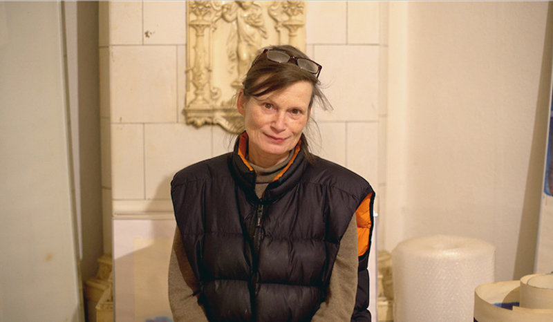 Hanna Frenzel, A petite woman stands in front of an old berlin style coal fireplace. 
