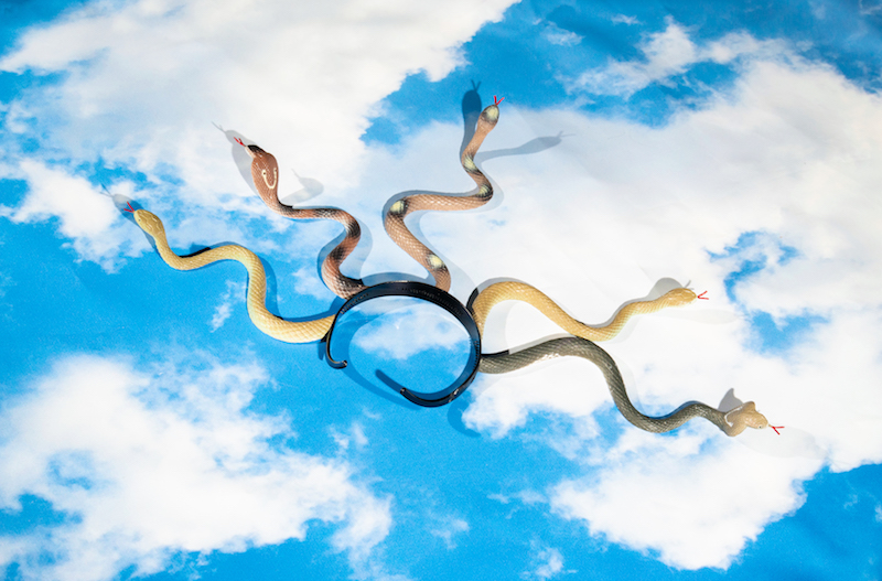 a headband with plastic snakes coming out of it, lies on top of a photograph of a blue cloudy sky