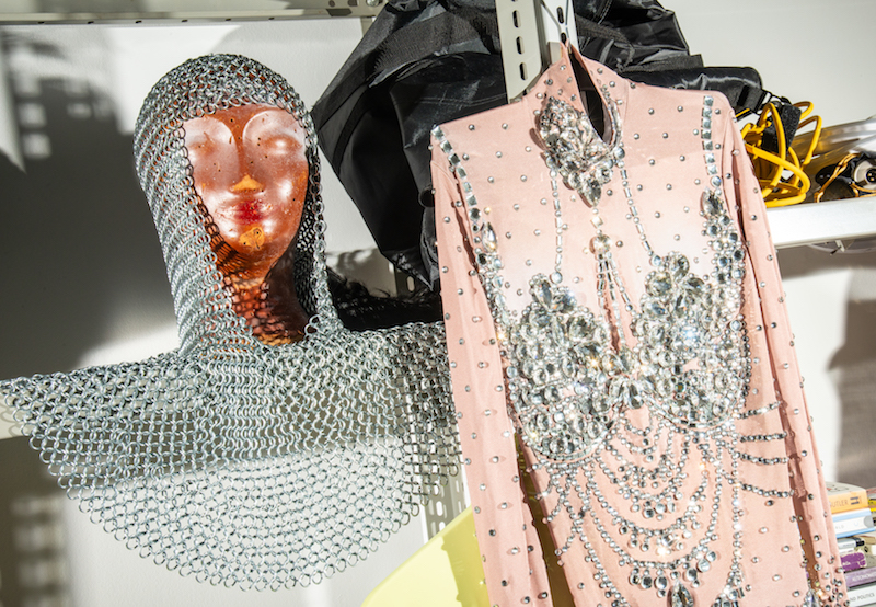 a chainmail hood and a sequined dress hang on a metal shelf