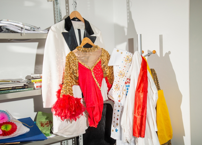 several costumes, including a dancer's sequined dress and a lounge suit, hang off of a metal shelf