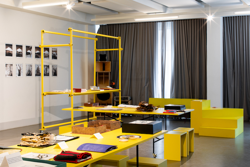 a curtained reading room with yellow bookshelves and seating around low yellow tables