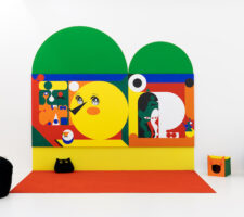 a vibrant wall installation in the white gallery space with bean bag chairs and cat houses on the floor