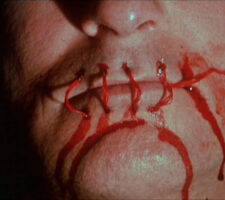 a close up of a person's mouth, with the lips sewn shut with bright red thread and a blood-like substance running down the cheeks and chin