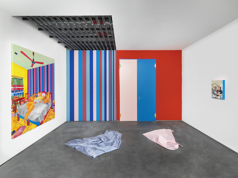 An installation view of the work The Chill (Mat, Elliot & Kevin in Zipolite),’ by Navot Miller, with the gallery wall having been painted in the same pattern and colors of the wall in the artist's painting.