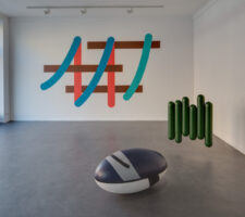 an installation view of the gallery's ground floor room with two colorful sculptures on the floor and a mounted abstract sign system