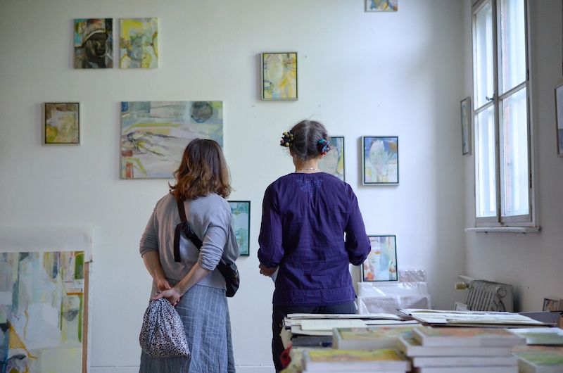 Two people seen from the back looking paintings hanging on a wall