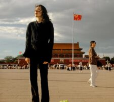 A woman standing on Tianamen square in Beijing with a cabbage on a leash