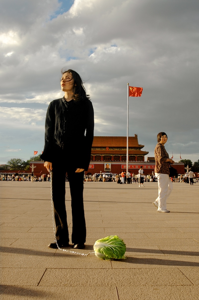 A woman standing on Tianamen square in Beijing with a cabbage on a leash