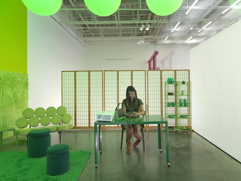 A woman looking at her phone sitting at table in a room with green furniture